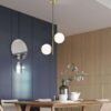 Modern nordic pendant light with two white globes shining brightly in sitting room. Replaces bulky chandeliers with sleek design.