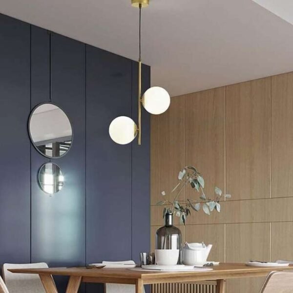 Modern nordic pendant light with two white globes shining brightly in sitting room. Replaces bulky chandeliers with sleek design.