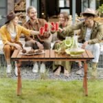 Group of friends using an aluminum picnic table outdoors for drinks and snacks.