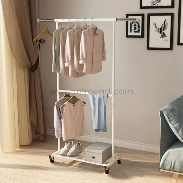 Extendible clothes rack with neatly hung shirts, pants, and shoes on the bottom shelf, placed in a bright room with wooden flooring.