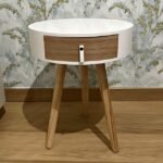 Modern bedside table with white round top and drawer by floral wall.