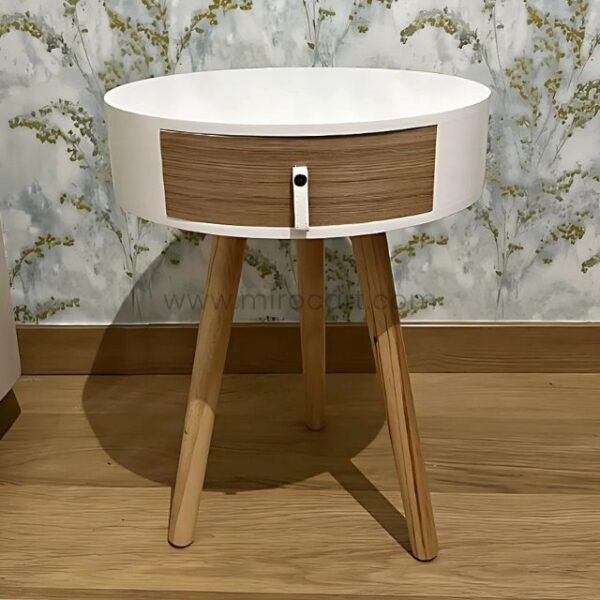 Modern bedside table with white round top and drawer by floral wall.