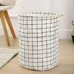 White laundry basket with black grid pattern and carry handles, placed on a wooden floor.