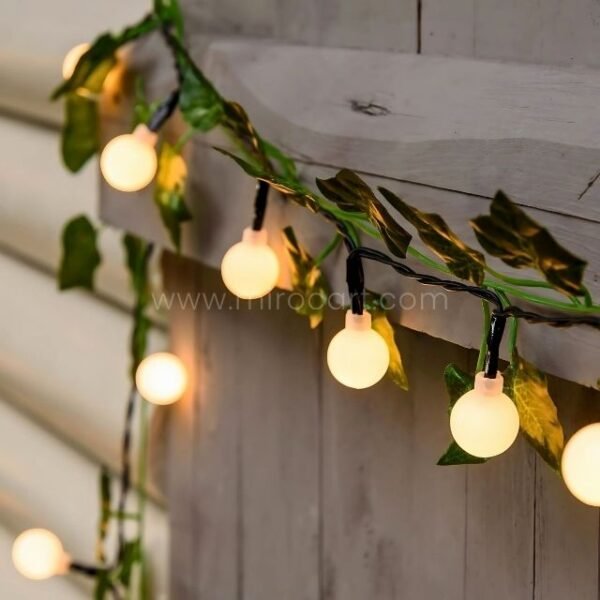 Warm white fairy lights intertwined with green artificial leaves, adding a nature-inspired touch to outdoor spaces.