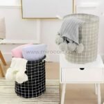 Black and grey storage baskets holding pastel pillows and pom-pom blankets in a tidy room setting.