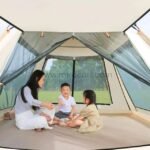 Spacious interior of an automatic camping tent with 600D oxford cloth floor and mesh windows. A family of four sits comfortably inside.