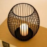 Spherical black lantern candle holder radiating golden light on a wooden table.