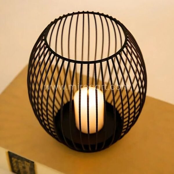 Spherical black lantern candle holder radiating golden light on a wooden table.