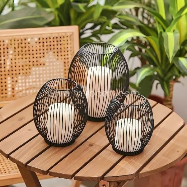 Three black wire lanterns on a wooden table with plants.