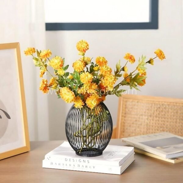 Black wire vase holding yellow flowers atop stacked books.