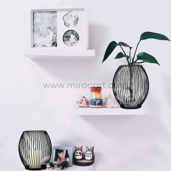 Black wire candle holder glowing on a minimalist wall shelf.