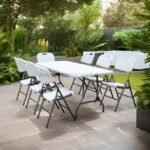 Folding chairs surrounding a white table on a patio with greenery. Durable and portable for outdoor use.