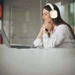 Woman wearing beige Green Lion Echo ANC Wireless Headphones while working at a desk, highlighting comfort and focus for work or leisure.