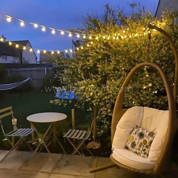 Outdoor patio with egg chair and table illuminated by globe string lights, creating a serene ambiance.