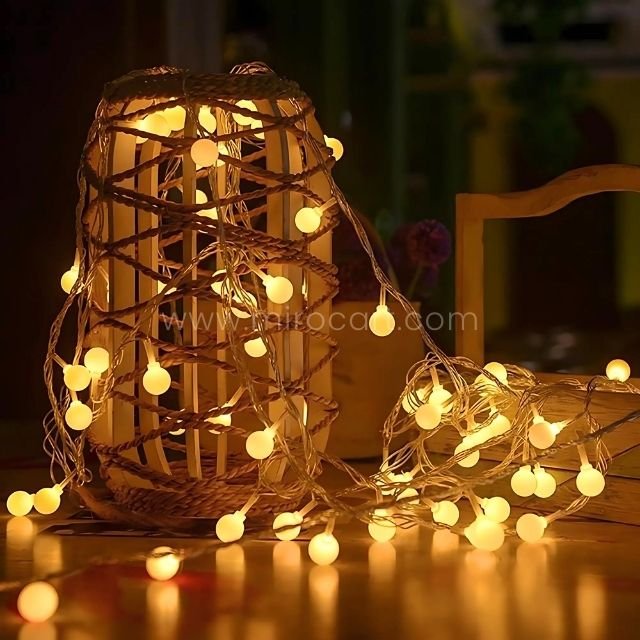 Wicker lantern wrapped in warm white globe string lights, creating a cozy glow for home decor.