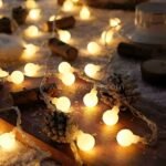 Globe string lights with pine cones on wooden surface, bringing festive warmth to holiday decor.