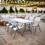 Folding chairs set for an outdoor banquet with tables under string lights. Portable and sturdy for formal events.