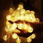 Hands gently cradling glowing warm white globe string lights against dark background.