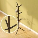 Tree branch coat hanger holding a hat and bag against a yellow wall.