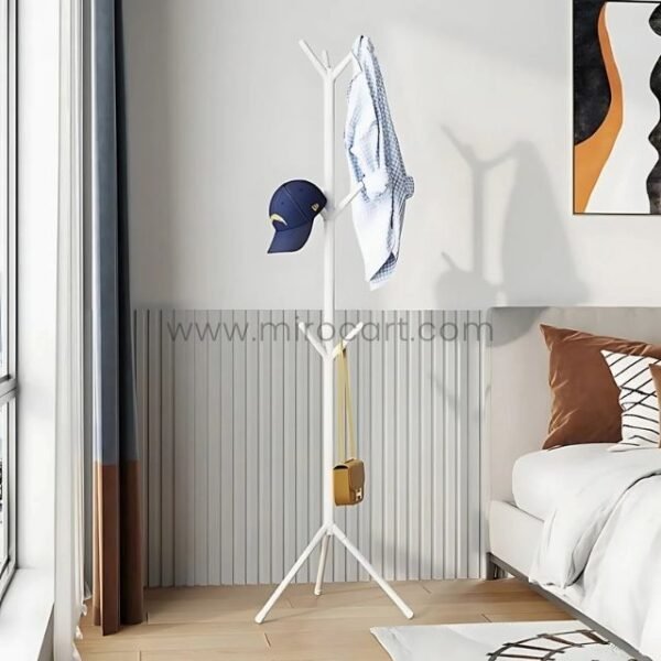 White tree branch coat hanger holding clothes in a bedroom with paneled walls.