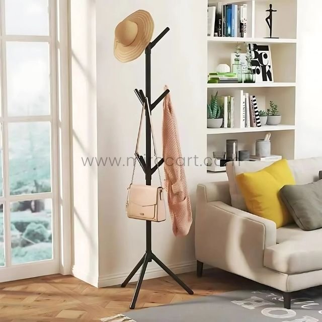 Minimalist tree branch coat hanger in a bright living room holding a hat, scarf, and handbag near a sofa with yellow cushions.
