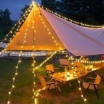 Globe string lights illuminating nighttime camping tent and table setup, creating a cozy outdoor atmosphere.