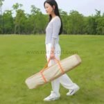 Woman holding a beige portable bag with orange handles, designed for carrying an automatic camping tent.