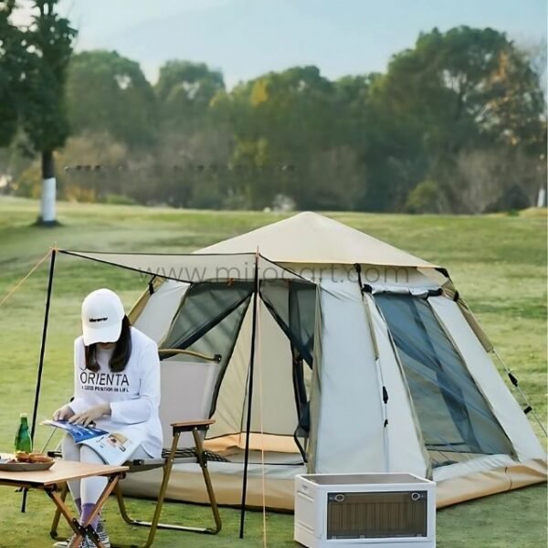 Woman sitting on a chair next to an automatic camping tent, reading a book with a portable cooler nearby.