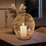 Gold lantern candle holder glowing beside pampas grass on wooden table.