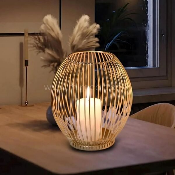 Gold lantern candle holder glowing beside pampas grass on wooden table.