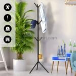 Black coat hanger near plants and decor items holding a cap and shirt.