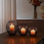 Black lantern candle holders of varying sizes glowing warmly on a table with floral decor.