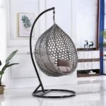 Modern grey rattan hanging egg chair with plush cushion and black steel frame in a cozy living room, featuring 360° swivel for ultimate relaxation