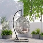 360° swivel grey rattan egg chair on black stand surrounded by lush patio greenery