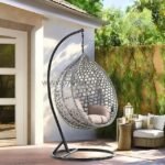 Outdoor hanging egg chair in grey rattan with black stand on sunny patio