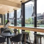 Nordic Cone Pendant Lamps in gray hanging above a cozy café seating area with large windows overlooking an urban view.