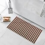 A textured non-slip bathroom mat placed on a tiled floor near a bathtub, soap dish, and showerhead.