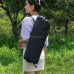 Woman carrying folded chair in storage bag.
