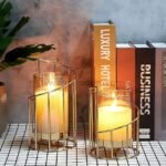 Golden pillar candle holders adding warmth to a bookshelf with classic novels.