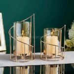 Golden pillar candle holders reflecting light dramatically on black polished surface.