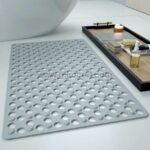 A gray non-slip massage bath mat placed near a bathtub on tiled flooring, with a wooden tray in the background.