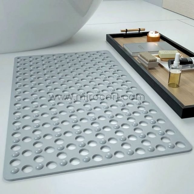 A gray non-slip massage bath mat placed near a bathtub on tiled flooring, with a wooden tray in the background.