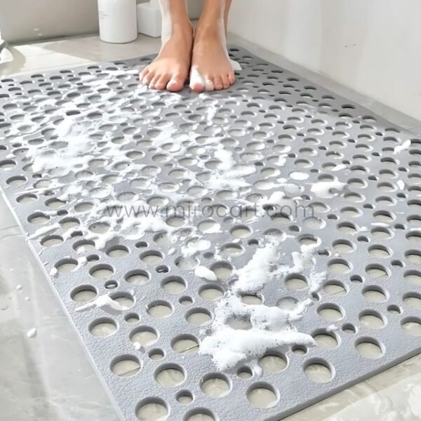 A woman standing barefoot on a gray non-slip massage bath mat inside a shower stall.