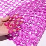 A close-up view of a pink non-slip shower mat with circular patterns, held by a hand to showcase its flexibility.