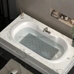 A clear bath mat placed inside a white bathtub filled with water.