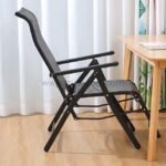 A premium zero-gravity lounge chair placed beside a wooden desk with a laptop, notebook, and pen nearby.