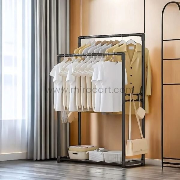 A sleek black space-saving clothes rack with neatly hung shirts and blouses, placed in a modern bedroom with wooden flooring and soft-toned curtains.