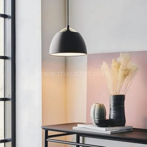 Sleek black Fjord Halo pendant light casts a warm ambient glow over a minimalist console in a modern living space.