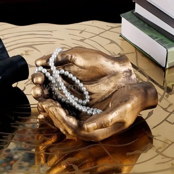 A bronze creative hand ashtray cradling a string of pearls on a reflective surface.