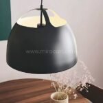 Black Fjord Halo pendant light glowing above a wood table with soft pink flowers, radiating warmth and elegance.